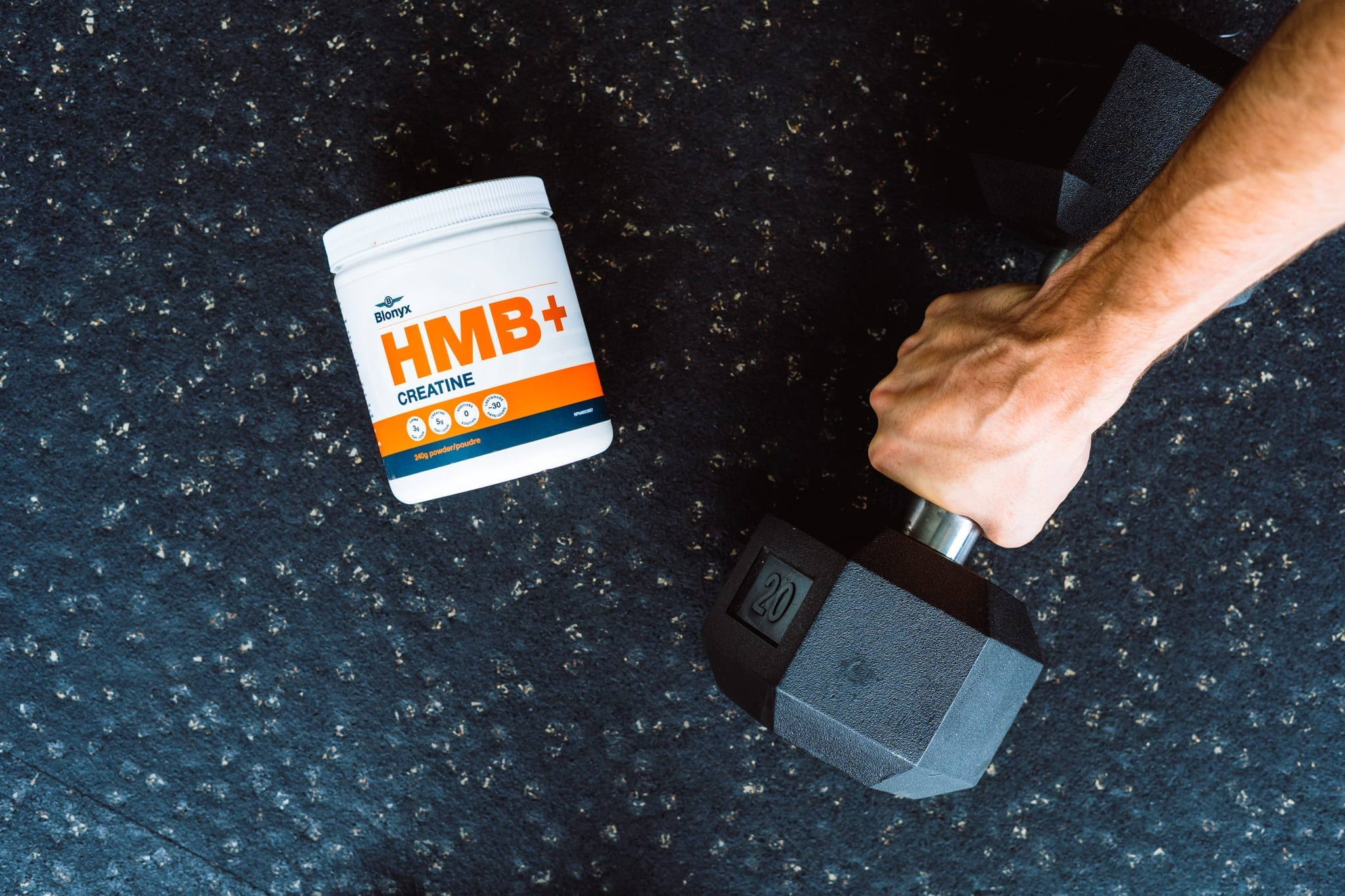 Blonyx HMB+ Creatine on a Gym Floor Next to Someone Picking up a Dumbbell