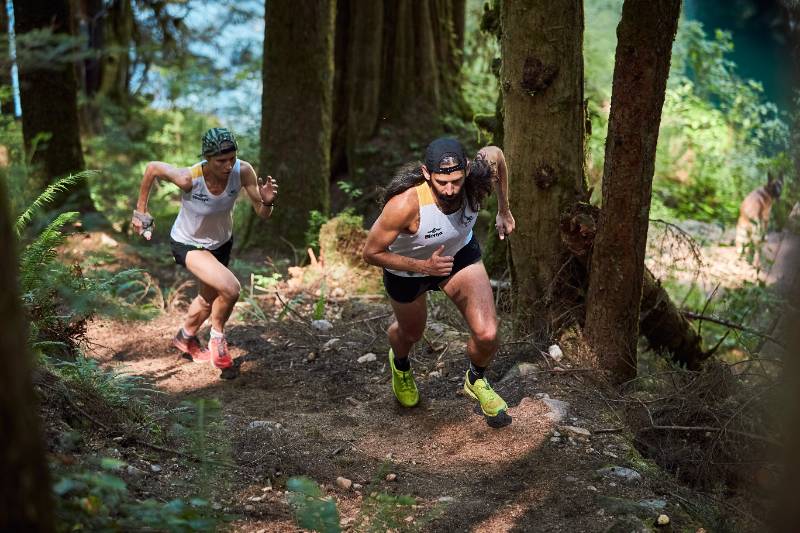 Trail runners climbing a steep forest trail during an endurance race, representing ultra running and exercise-associated muscle cramps.