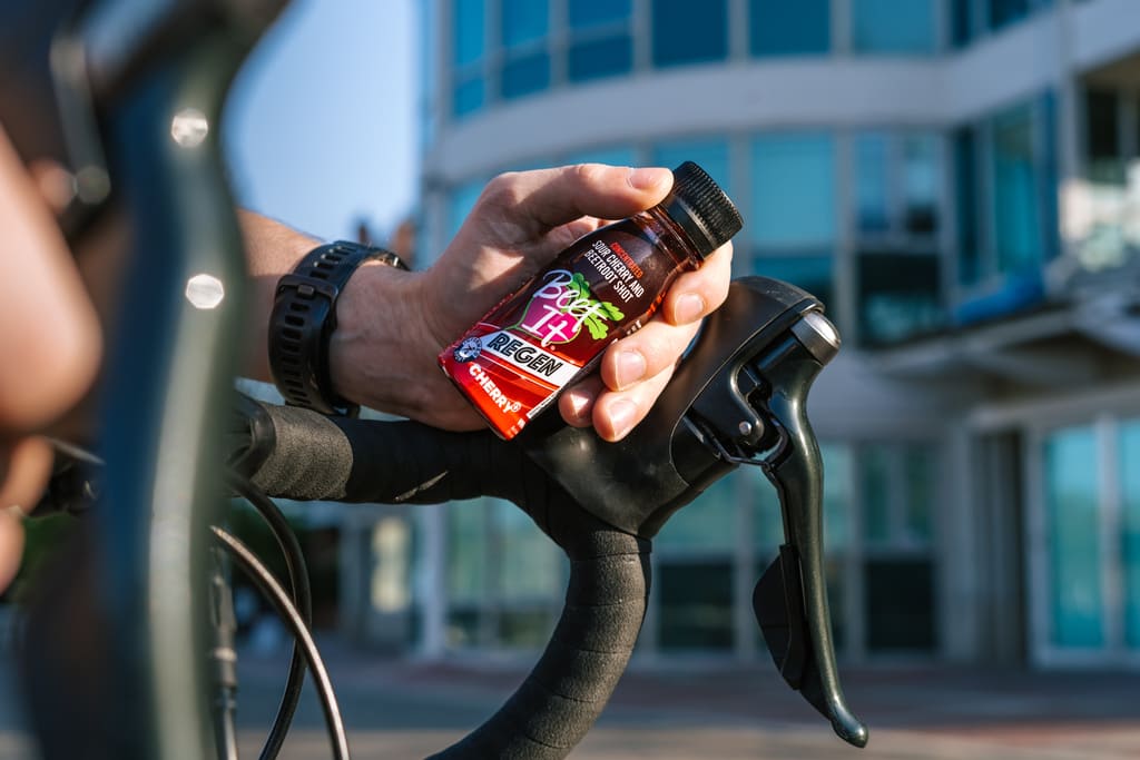 Cyclist holding a shot of Beet It Regen Cherry+ over their handle bars
