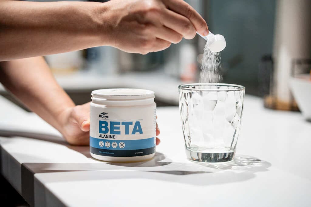 Person adding a scoop of Blonyx Beta Alanine to a glass
