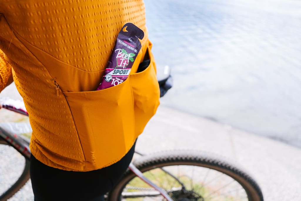 Cyclist wearing a yellow jacket with a Beet It Sport Top Up 100 gel in the pocket