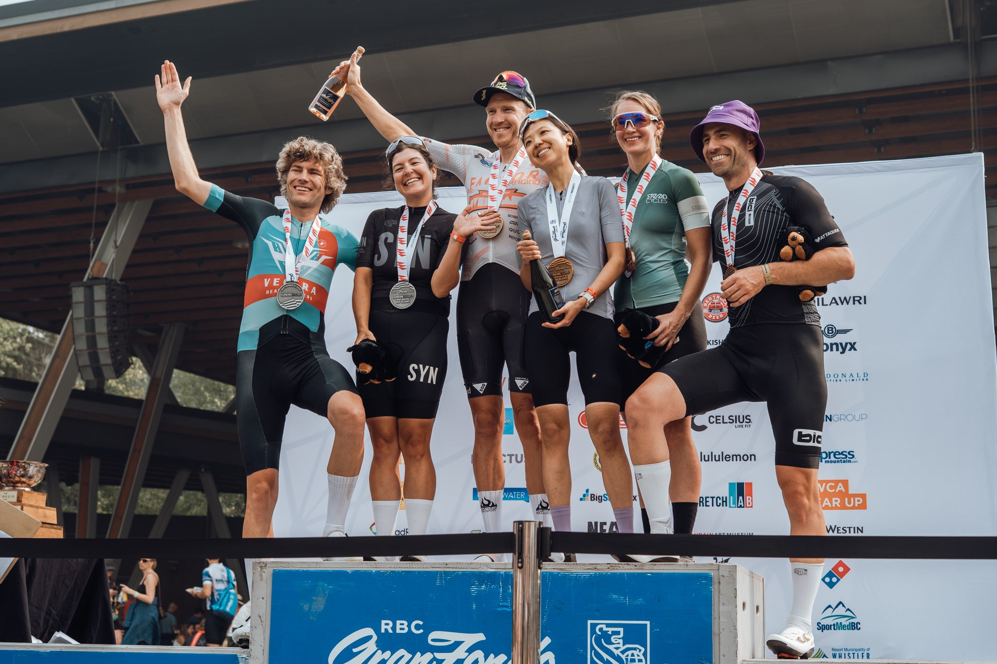 Group of cyclists celebrating on a podium with trophies and medals.