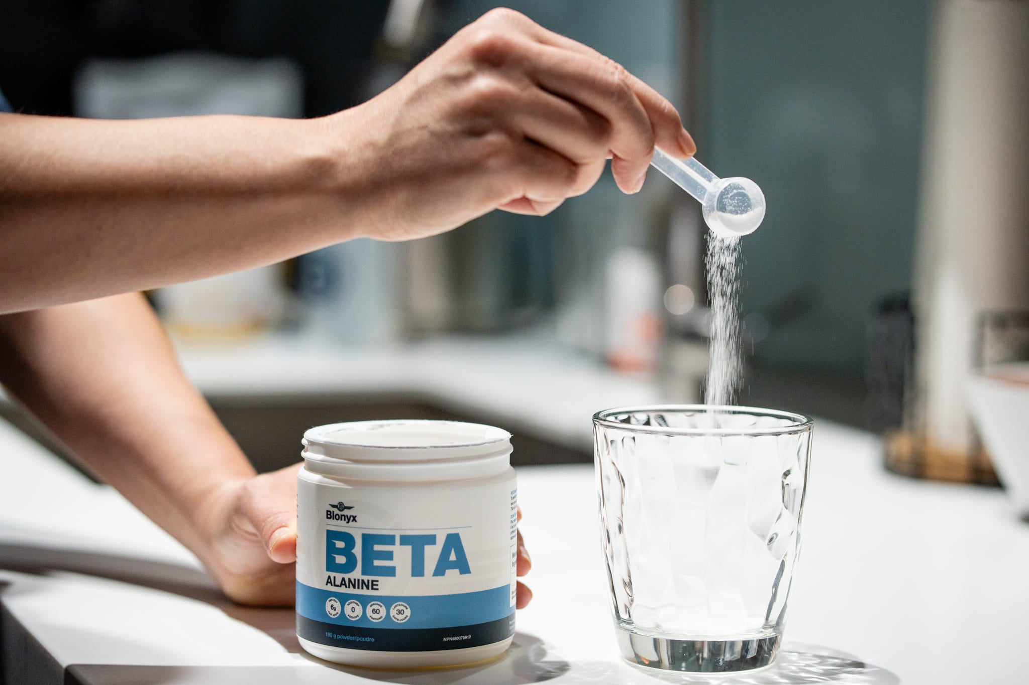 A person adding a scoop of Blonyx Beta Alanine to a glass.