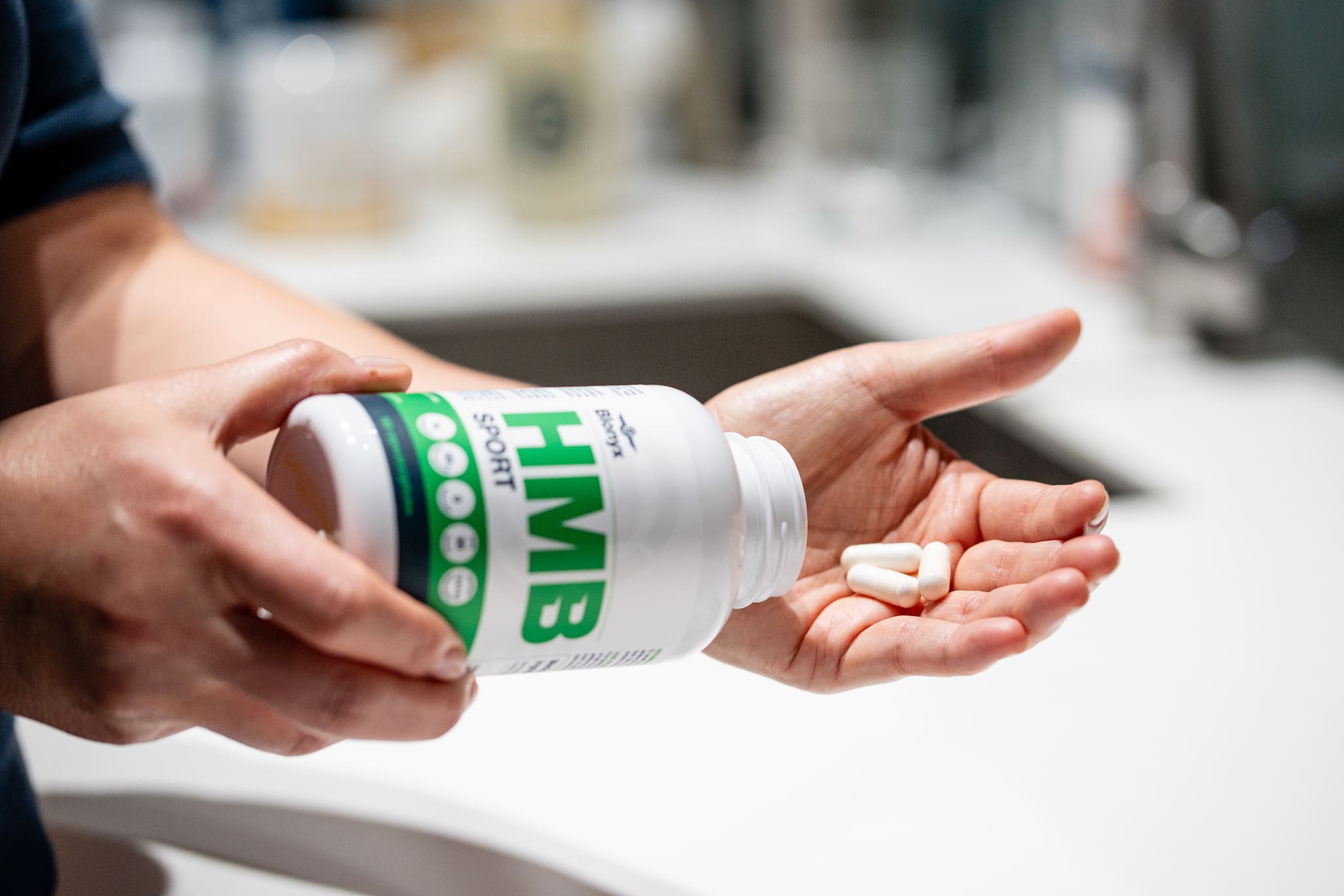 A person pouring Blonyx HMB Sport capsules from the bottle.